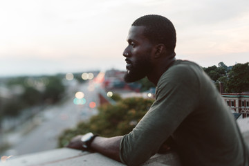 A young man posing on a roof overlooking the city at sunset