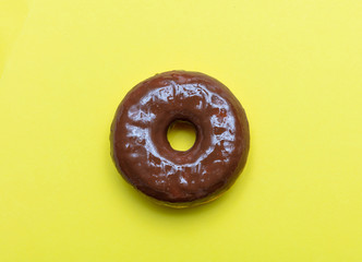 Chocolate doughnut on yellow color background, top view