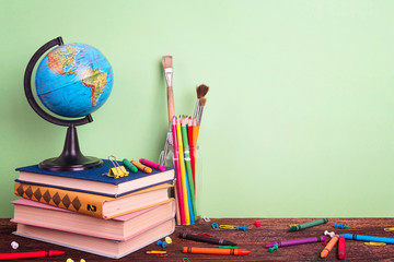Education composition with a globe, a stack of books and school supplies on a green background. Copy space for text.