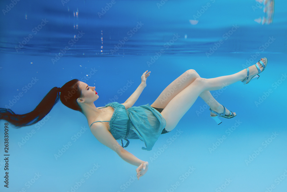 Wall mural surreal, concept, art portrait of beautiful gorgeous brunette young woman with make up underwater in the swimming pool on blue background  - Wall murals