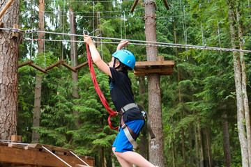boy in equipment (helmet, safety rope) walking high up the rope climbing with safety system in an adventure park 