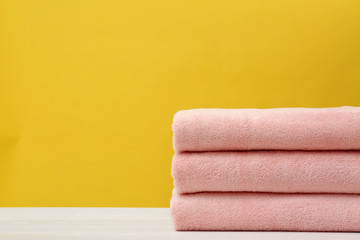 Stack of soft clean towels on table against color background. Space for text