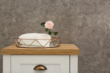 Rolled soft towel with beautiful flower in decorative tray on chest of drawers. Space for text