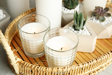 Wicker tray with burning candles and houseplants on table