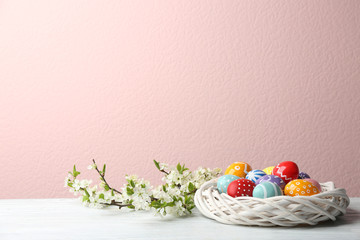 Fototapeta na wymiar Painted Easter eggs in nest and blossoming branches on table against color background. Space for text