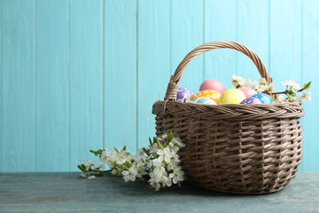Fototapeta na wymiar Painted Easter eggs in wicker basket and blossoming branches on table against color background. Space for text