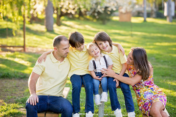 Beautiful family, mother, father and three kids, boys, having familly outdoors portrait taken on a sunny spring evening, beautiful blooming garden, sunset time