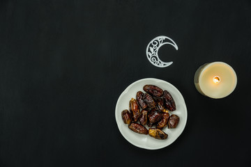Table top view aerial image of decoration Ramadan Kareem holiday background.Flat lay date with rosary & lighting candle and moon.Essential objects on modern rustic black wooden.Space for design.