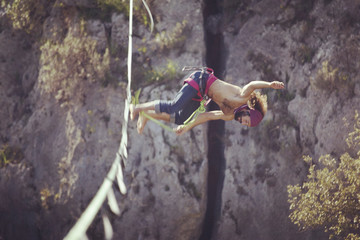 A man is walking along a stretched sling. Highline in the mountains. Man catches balance. Performance of a tightrope walker in nature. Highliner on the background of valley.