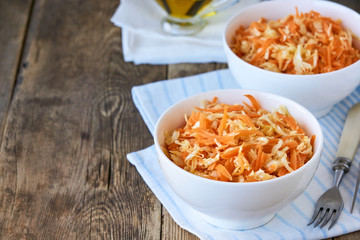 Salad with fresh cabbage, carrots and olive oil in a white bowl on a wooden background 