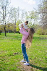 Obraz premium Mom with baby in bright clothes on a pink plaid on the green right. Family resting in the park on a warm day. Mom and little girl 10 months walk in the park