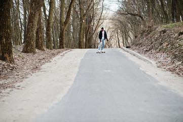 Street style arab man in eyeglasses with longboard longboarding down the road.
