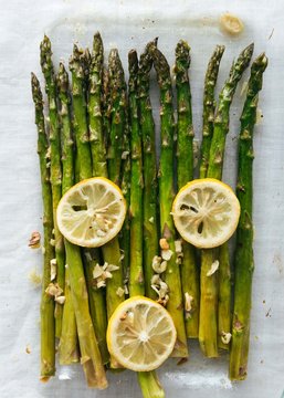Roasted asparagus, lemon, garlic on ceramic plate and linen tablecloth