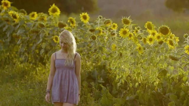 Medium shot of a girl walking in front of sunflowers in slowmotion