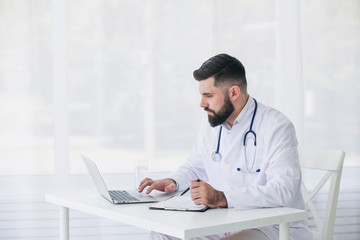Doctor is working with documents and laptop in his medical office
