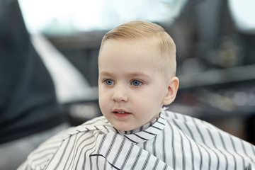 Cute blond smiling baby boy with blue eyes in a barber shop after haircut by hairdresser. Children...