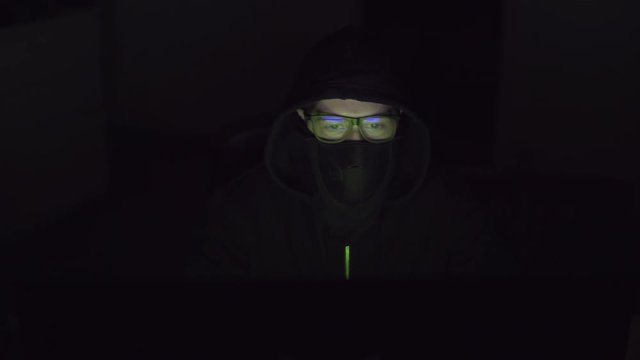 Hacker with a covered face is working on the computer.