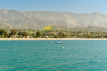 Obraz premium Santa Barbara Seashore o poranku. Łódź na wodzie, piękna plaża z palmami i góry na horyzoncie