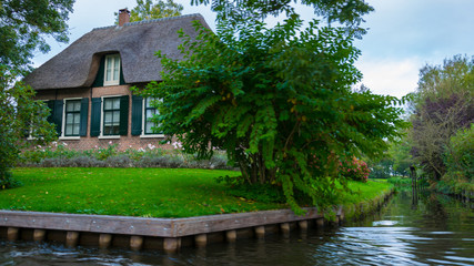 A house in Giethoorn, the Netherlands, photographed on water channels on a fall day, with green grass, and special architecture of the area.