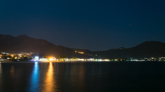 night view over the thassos island in Greece, the skala potamia village, with lights on the cliff, clear sky, stars in the sky and sea water as a mirror