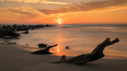 sunrise seen from the sand, with long exposure and the sea like a mirror, stones coming out of the...