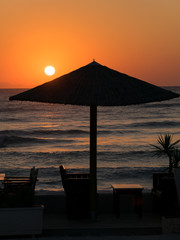 sunrise on the seafront with reed sun silhouette umbrellas, the sea with waves and dinner table.