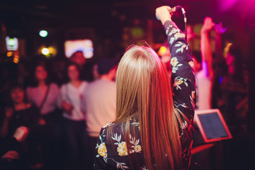 Beauty model girl singer with a microphone singing and dancing over holiday glowing background. Karaoke party singer. Disco party. Celebration.