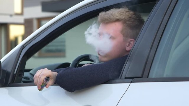Addiction concept. Millennial man vaping while sitting in car