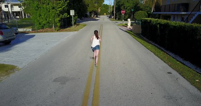 Angled down over a girl as she runs through the streets of Key Largo, Florida on a bright and sunny day.