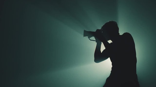 A Photographer Moves Around and Takes Pictures Actively in Silhouette. Dark Background.