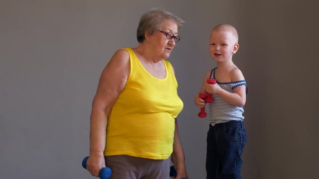 Elderly woman grandmother in yellow shirt doing gymnastics with dumbbells with grandchild