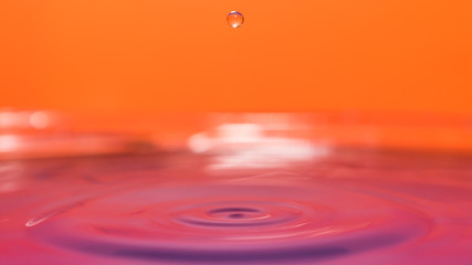 water splash in colorful background with a drop of water flying from above