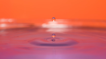 water splash in colorful background with a drop of water flying from above