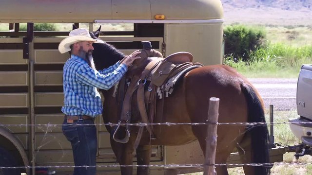 Slow pan around Rancher as he saddles thoroughbred horse for ride in country