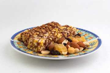 vegan dessert: several cereal bars with raisins and honey are on a bright plate, a lot of nuts and candied fruits are lying around, short focus