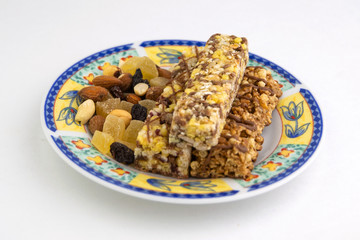 vegan dessert: several cereal bars with raisins and honey are on a bright plate, a lot of nuts and candied fruits are lying around, short focus