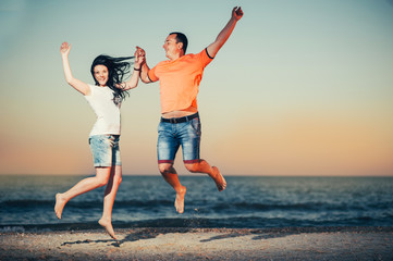 happy Young couple of lovers man and jump and laughing on the seashore on sunset. Love near sea. Emotions Summer Lifestyle People Feelings Travel Anniversary Happiness