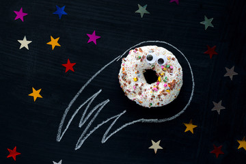 donut meteorite with googly eyes among the stars  on a black chalkboard background, funny...