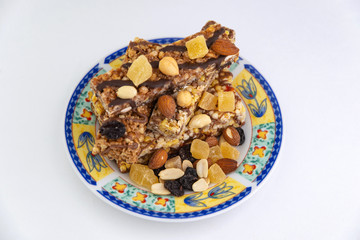 vegan dessert: several cereal bars with nuts, raisins and honey, in a colorful plate on white, short focus