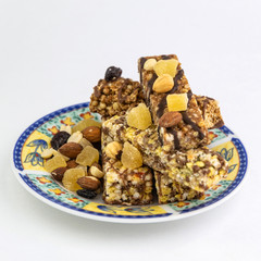 vegan dessert: several cereal bars with nuts, raisins and honey, in a colorful plate on white, short focus
