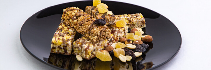 vegan diet: several cereal bars with nuts, raisins and honey, in a black plate on white, short focus