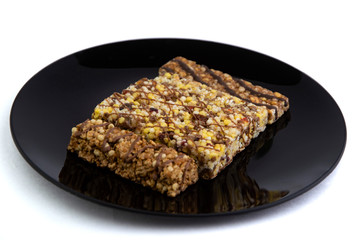 vegan diet: several cereal bars with raisins and honey, in a black plate on white, short focus