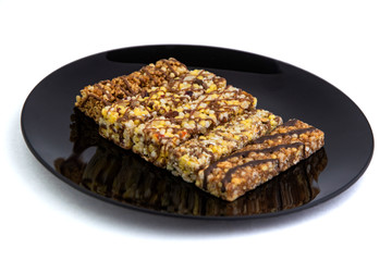 vegan diet: several cereal bars with raisins and honey, in a black plate on white, short focus
