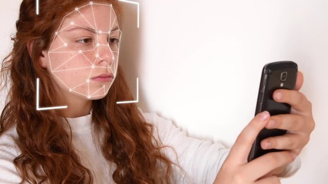 Close up of a young woman with red hair, with a white shirt on a white background, while holding a phone in front of her face with facial recognition high tech animation with a glow effect on her face
