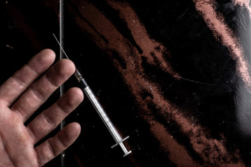 heroin intoxication: a syringe is lying next to the hand of a young guy on a dark table