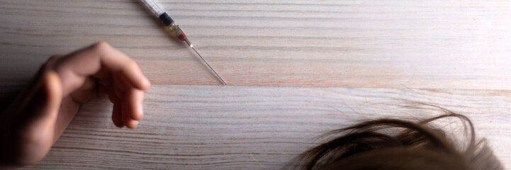 heroin overdose: a syringe is lying next to the hand of a young guy on the table