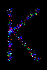 The letter "K" of the English alphabet made of multicolored electric garlands on a dark background, blur, bokeh, isolated on black