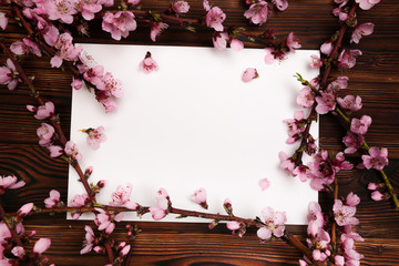 White paper sheet and sprigs of the apricot tree with flowers on wooden background. Place for text. The concept of spring came, happy easter, mother's day.Top view.Flay lay. Copy space.