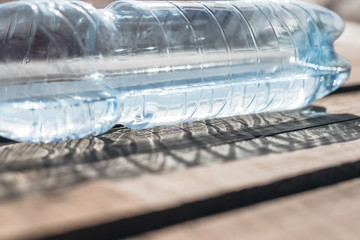 Plastic bottle with mineral water lies on a wooden surface. The sun's rays shine through the water, forming an abstract pattern on the boards.