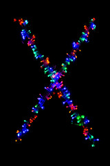 The letter "X" of the English alphabet made of multicolored electric garlands on a dark background, blur, bokeh, isolated on black